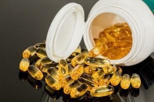 Golden-yellow translucent liquid gel capsules spilling out of an open white bottle onto a reflective dark surface